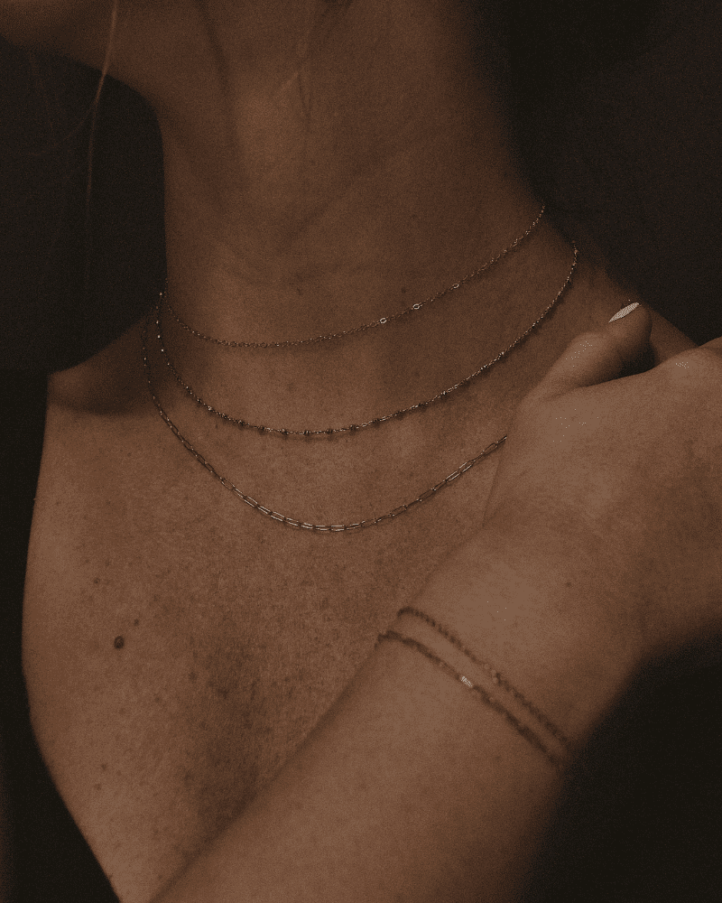 Close-up of a woman wearing gold necklaces and a bracelet, showcasing elegant minimalist jewelry.