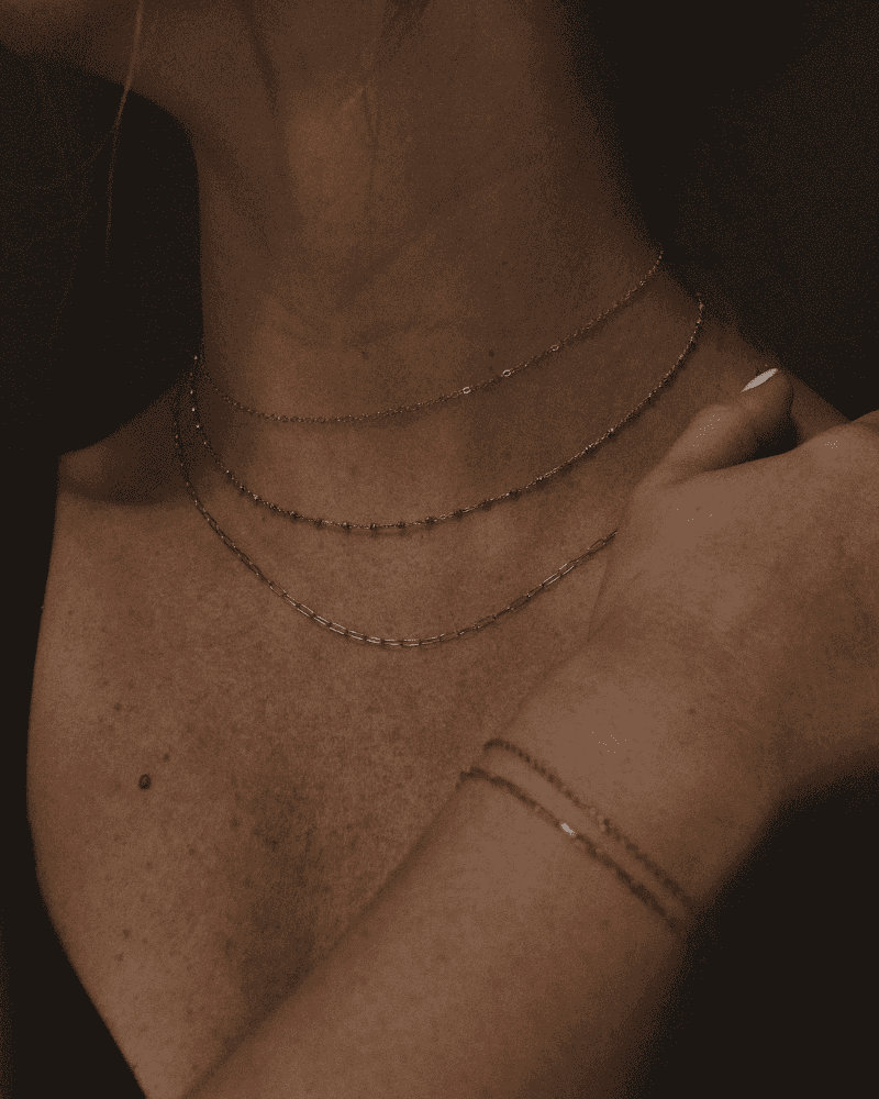 Close-up of a woman wearing gold necklaces and a bracelet, showcasing elegant minimalist jewelry.