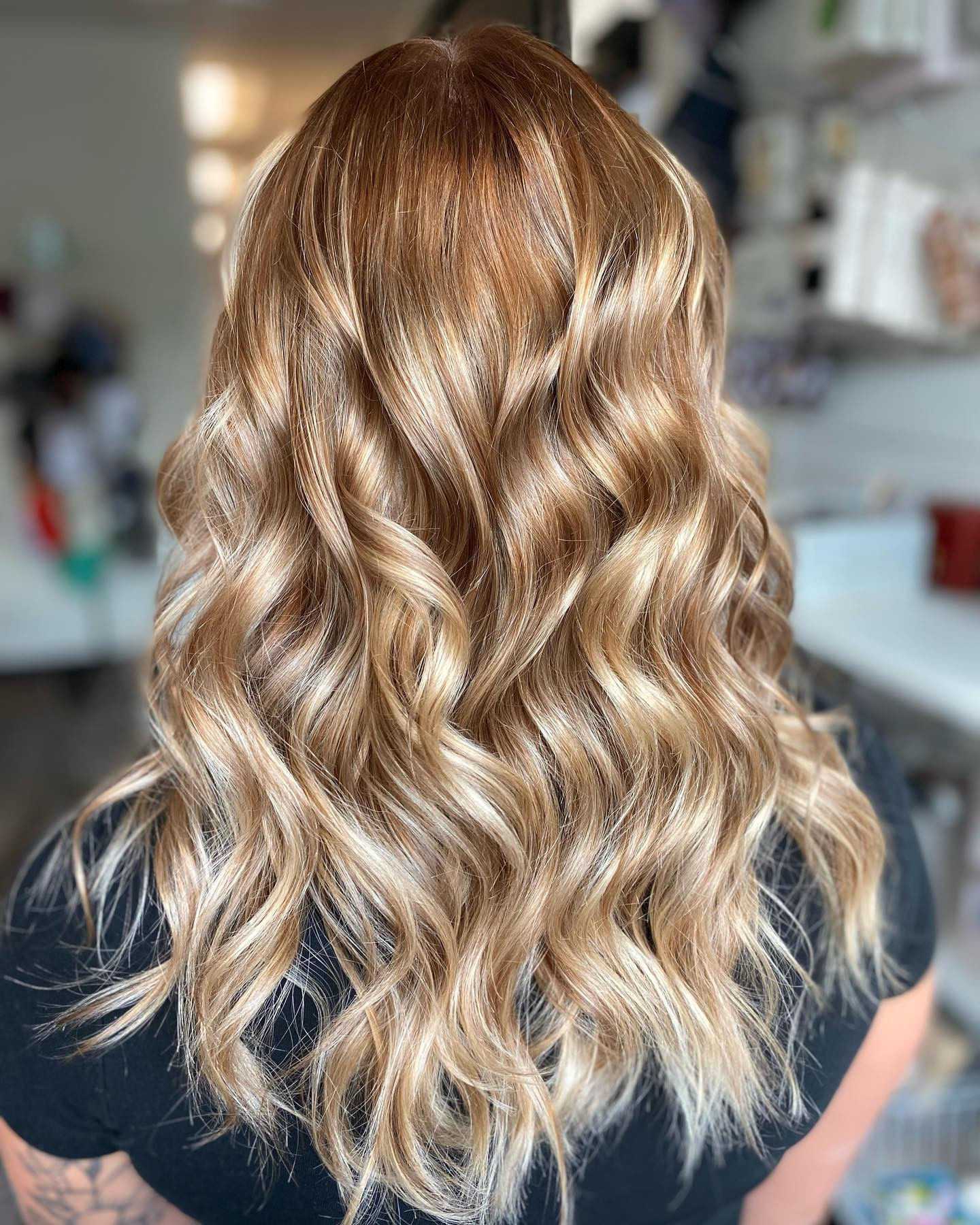 Back view of a person with wavy, shoulder-length, blonde hair in a well-lit room.